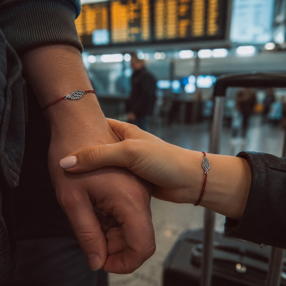 Couple holding hands at the airport wearing matching red cord wing bracelets — Second Wing set