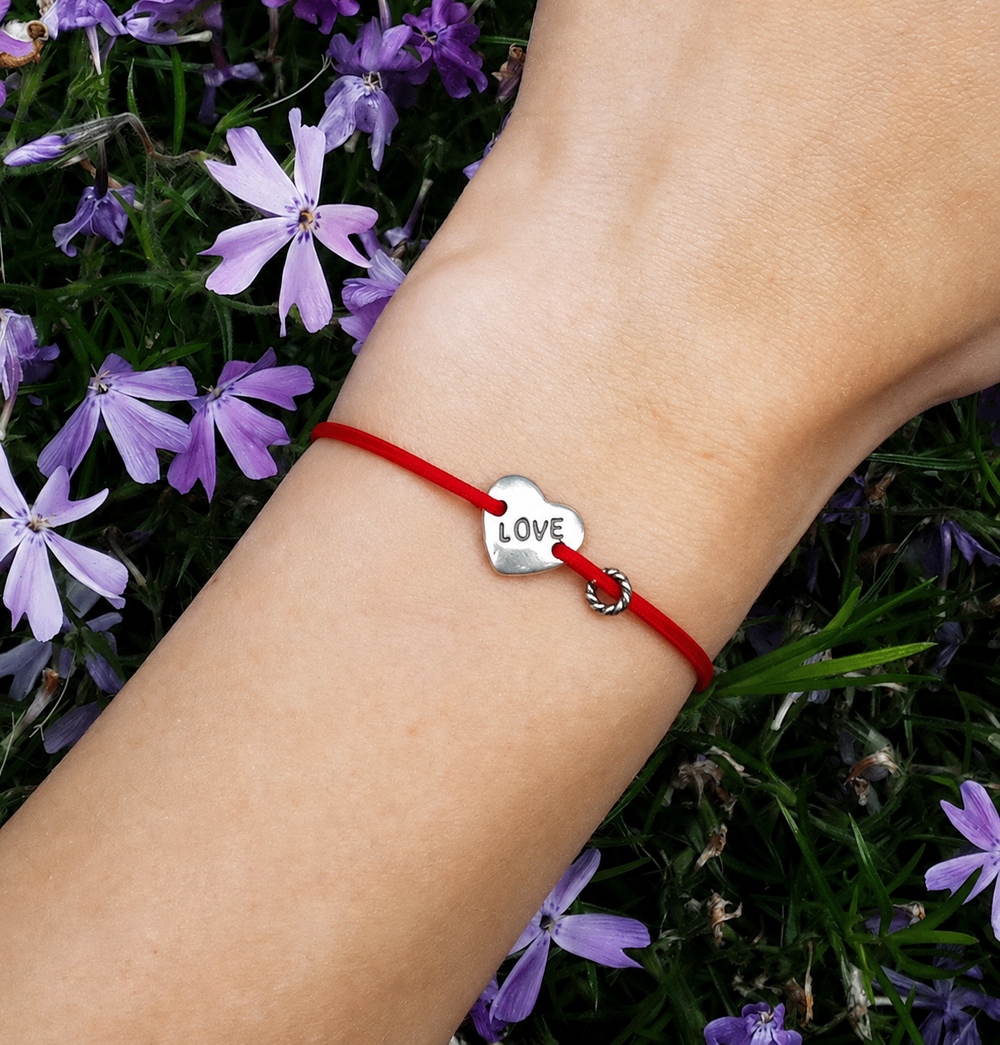 Love Bracelet on a red cord, worn on the wrist among spring flowers