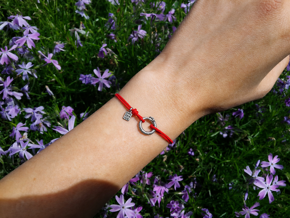 Ouroboros Bracelet on a red cord, worn among spring flowers
