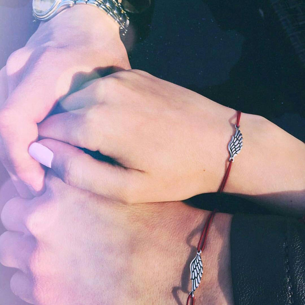 Couple holding hands wearing matching red cord wing bracelets — Second Wing set