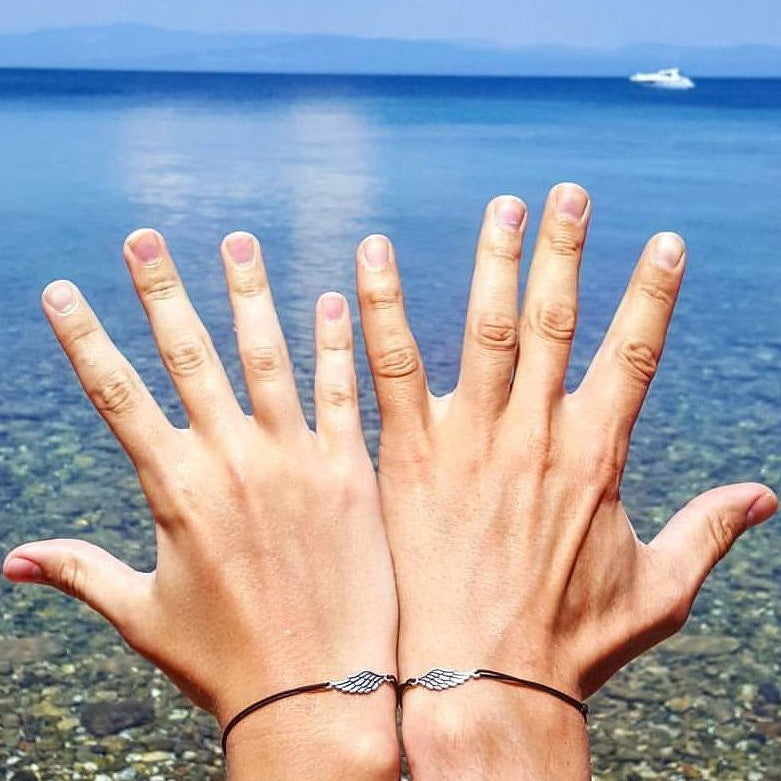 Two hands by the sea wearing matching wing bracelets — Second Wing set